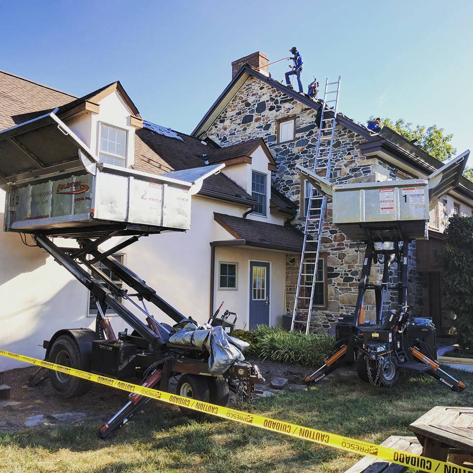 caution tape, machinery, and ladder in front of house with roofers on the roof