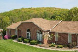 brick house in front of forest with shake asphalt shingles on roof