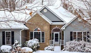 House with snow on roof surrounded by snowy trees and bushes
